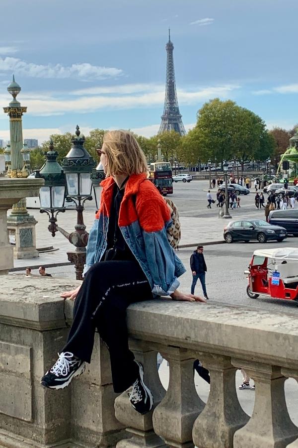 Io seduta nel parco dei Giardini delle Tuileries a Parigi, di fronte a Place de la Concorde, mentre ammiro la Torre Eiffel in lontananza in una giornata primaverile dal cielo sereno. Indosso un look streetwear, immersa nell'atmosfera parigina.