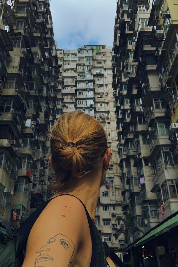 Io di spalle al Monster Building di Hong Kong, catturata in un'atmosfera misteriosa con luce scura e un'inquadratura suggestiva dal basso, che enfatizza le linee architettoniche e i toni profondi dell'ambiente urbano.