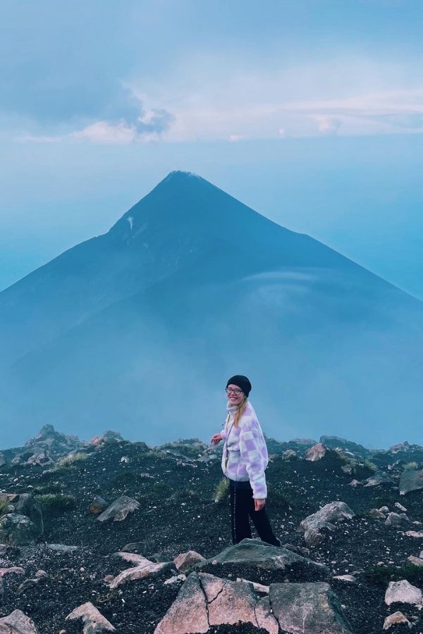 Ritratto all'alba in Guatemala dopo la scalata del vulcano Acatenango, con vista mozzafiato sul vicino vulcano attivo Fuego. La luce del mattino illumina il panorama vulcanico, creando un'atmosfera unica e suggestiva sui toni del blu. 